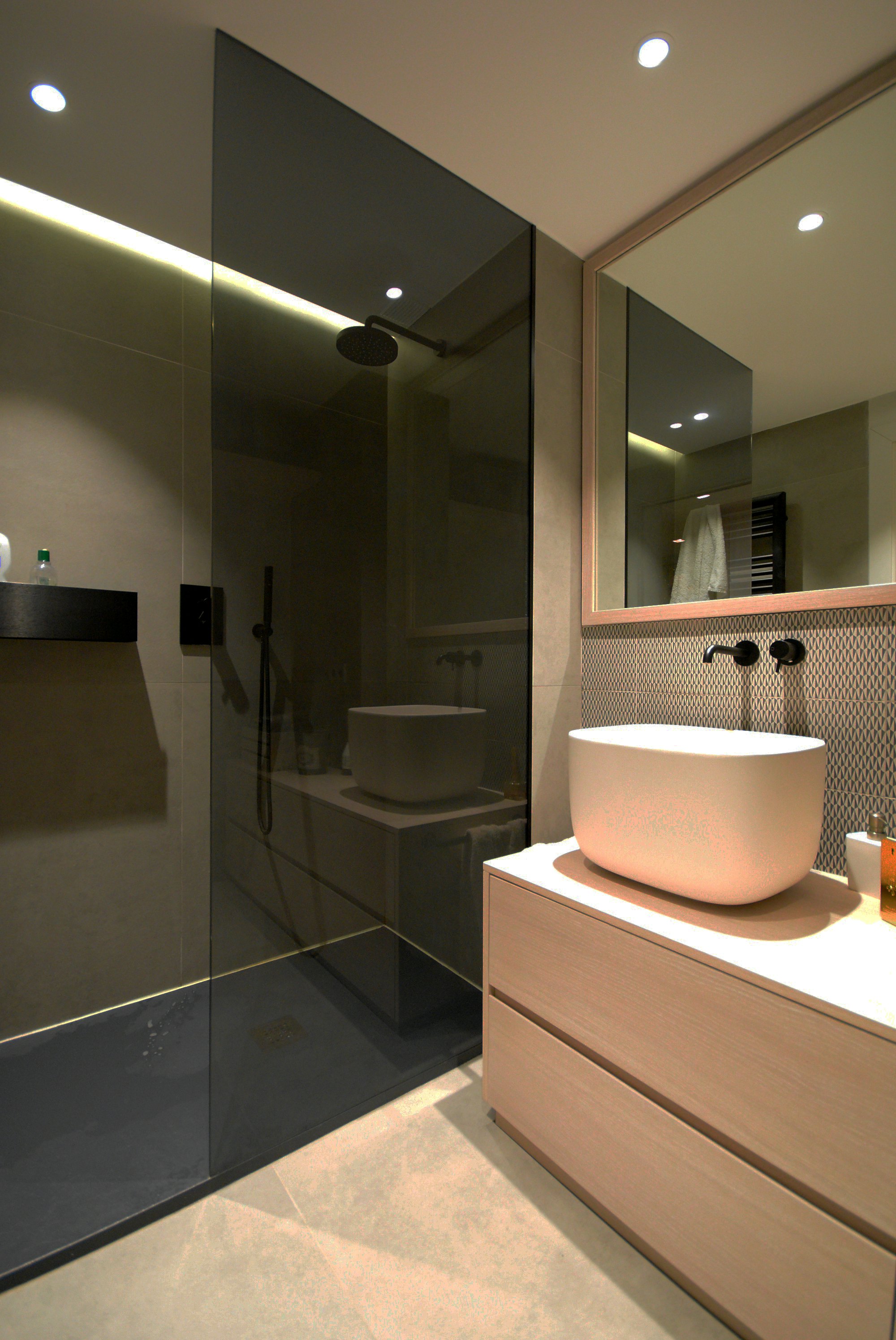 Dark bathroom with a sculpted stone vessel basin, black wall taps and warm light